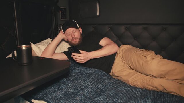 Tired truck driver falling asleep with smartphone in his sleeper cab