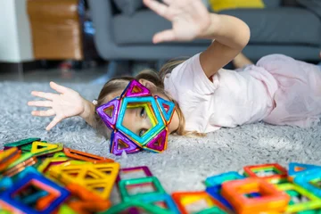 Young girl playing on carpet with colorful magnetic building tiles © Алина Бузунова
