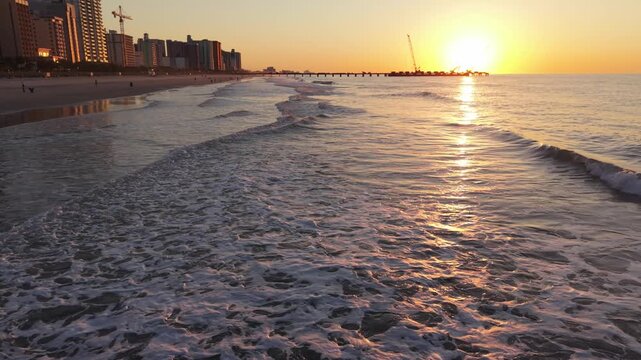 Waves roll onto the sandy beach at sunset, showcasing a picturesque skyline and pier in Myrtle Beach, South Carolina, USA