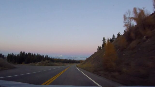Driving toward Grand Teton mountains on Highway 287 at sunrise