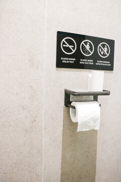 A black public restroom sign with explicit rules mounted above a metal toilet paper holder