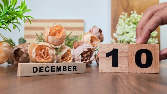 Hand placing wooden calendar blocks showing december 10 on a wooden table