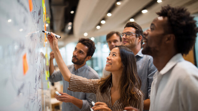 Diverse team brainstorming and collaborating with markers on a whiteboard, conceptualizing ideas, perfect for business meetings, creative workshops and team building activities