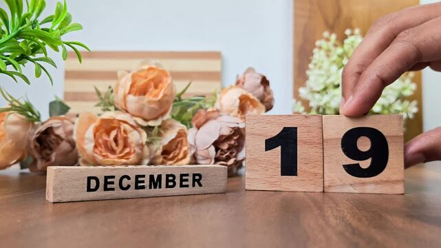 Hand placing wooden calendar blocks showing december 19 on a wooden table