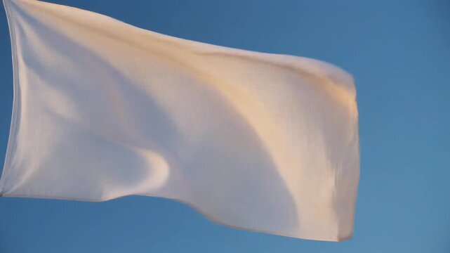 Plain white flag waving gently in the bright blue sky captured in a cinematic motion video