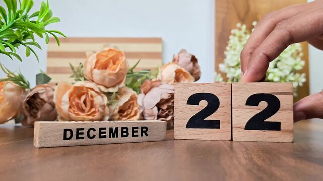 Hand placing wooden calendar blocks showing december 22 on a wooden table