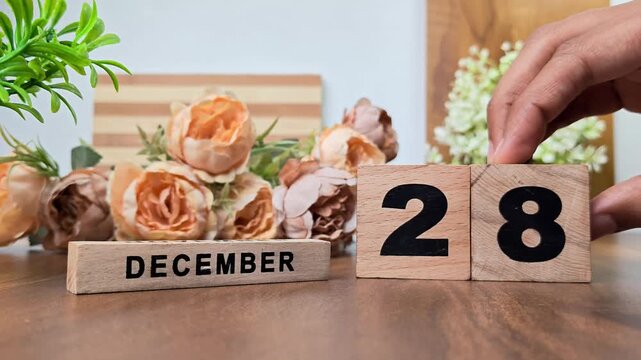 Hand placing wooden calendar blocks showing december 28 on a wooden table