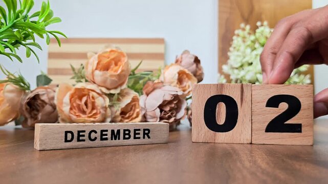 Hand placing wooden calendar blocks showing december 2 on a wooden table