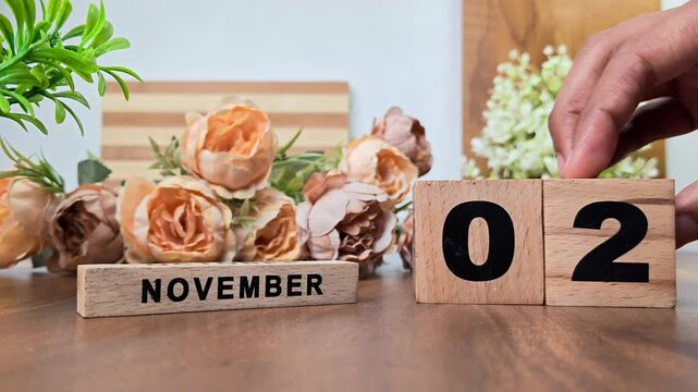 Hand placing wooden calendar blocks showing november 2 on a wooden table