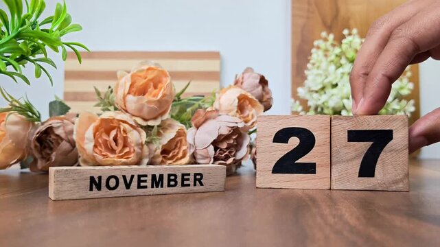 Hand placing wooden calendar blocks showing november 27 on a wooden table