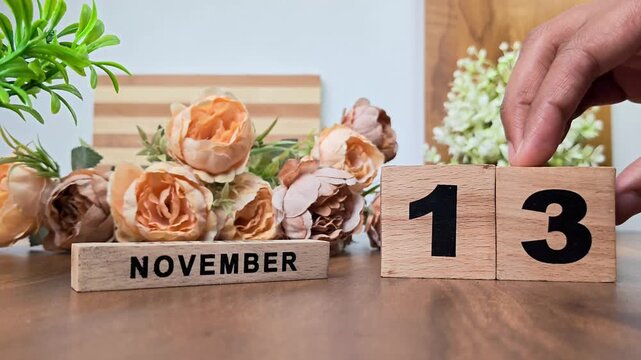 Hand placing wooden calendar blocks showing november 13 on a wooden table
