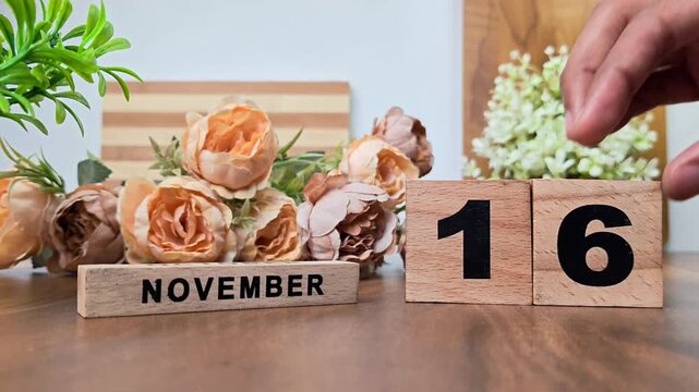Hand placing wooden calendar blocks showing november 16 on a wooden table