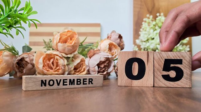 Hand placing wooden calendar blocks showing november 5 on a wooden table