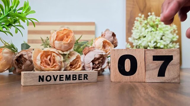 Hand placing wooden calendar blocks showing november 7 on a wooden table