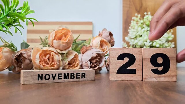 Hand placing wooden calendar blocks showing november 29 on a wooden table