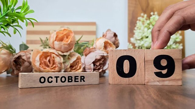Hand placing wooden calendar blocks showing october 9 on a wooden table