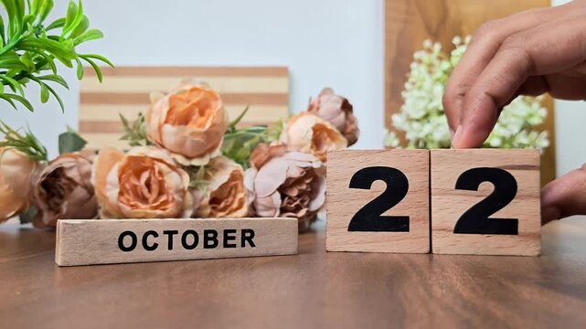 Hand placing wooden calendar blocks showing october 22 on a wooden table