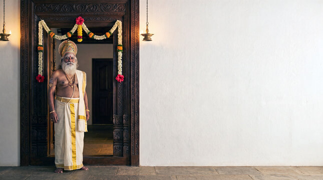 A man dressed as King Mahabali standing in a traditional Kerala-style decorated doorway, with copy space for text on the wall.