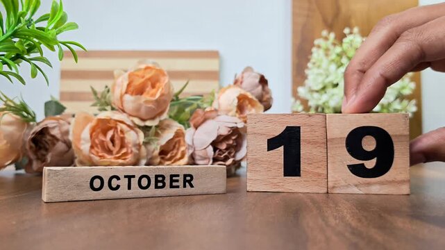 Hand placing wooden calendar blocks showing october 19 on a wooden table