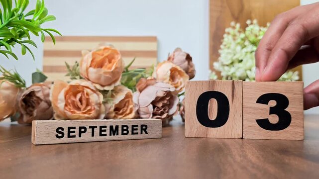 Hand placing wooden calendar blocks showing september 3 on a wooden table