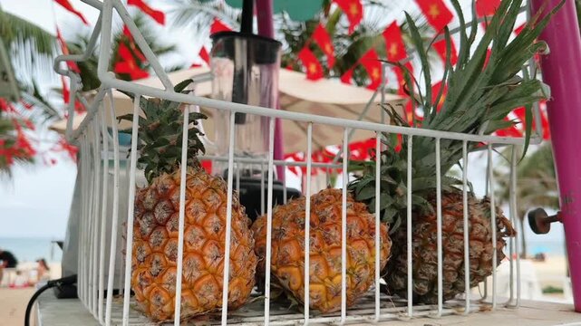 Close up of Fresh Pineapples in Wire Basket with Blender at Beach Smoothie Stand