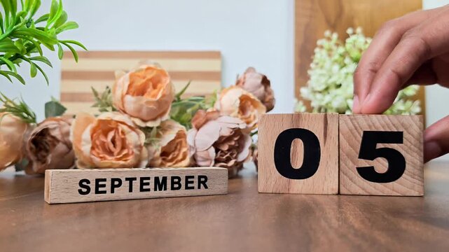 Hand placing wooden calendar blocks showing september 5 on a wooden table