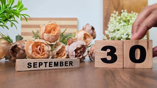 Hand placing wooden calendar blocks showing september 30 on a wooden table