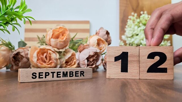 Hand placing wooden calendar blocks showing september 12 on a wooden table