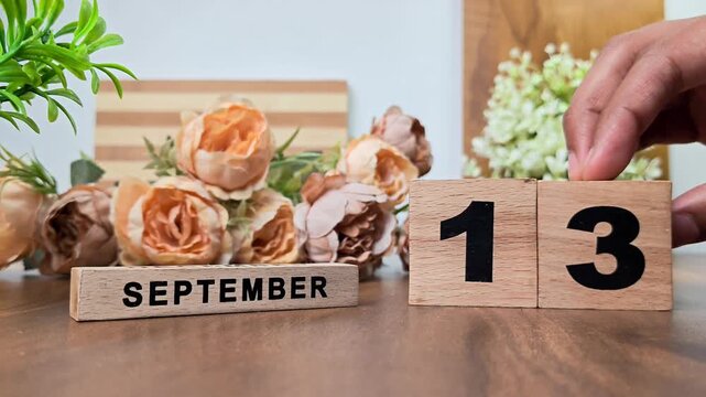 Hand placing wooden calendar blocks showing september 13 on a wooden table