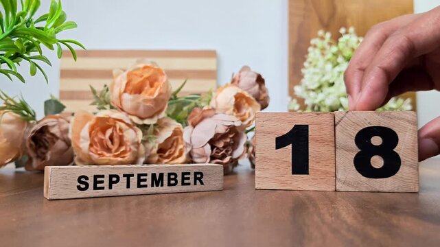 Hand placing wooden calendar blocks showing september 18 on a wooden table