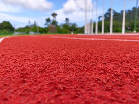 Macro texture of red rubber running track surface with shallow depth of field in stadium.