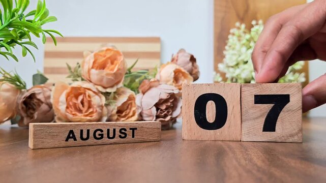 Hand placing wooden calendar blocks showing august 7 on a wooden table