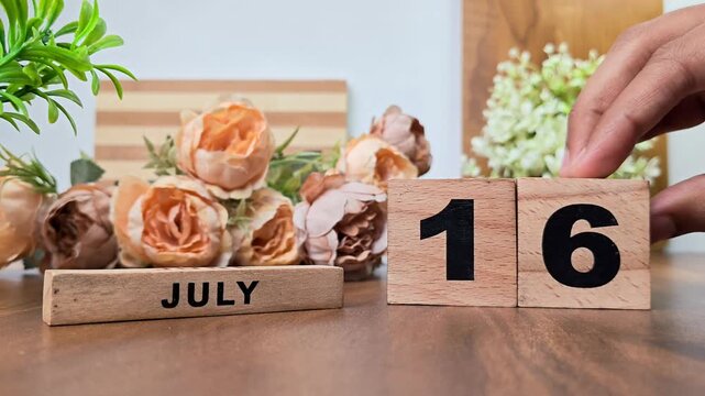 Hand placing wooden calendar blocks showing july 16 on a wooden table