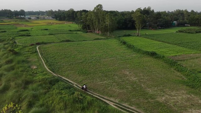 Rural landscape aerial view two people riding motorcycle on dirt path through lush green