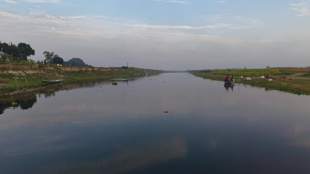 Serene river landscape with gentle reflections and distant village life under a calm sky