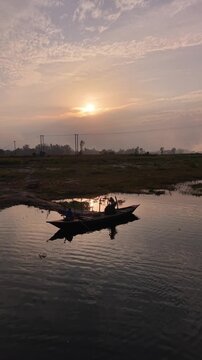 Serene sunrise over calm water with silhouette of person rowing small boat peaceful rural