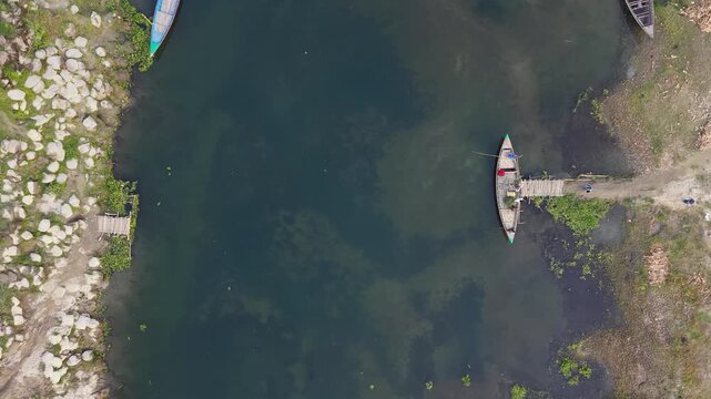 Aerial drone view of traditional wooden boat docked at a rustic pier on a calm river with lush