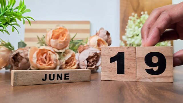 Hand placing wooden calendar blocks showing june 19 on a wooden table