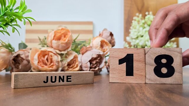 Hand placing wooden calendar blocks showing june 18 on a wooden table
