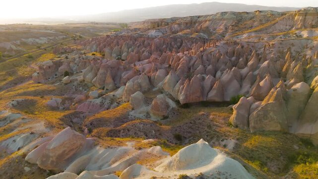 Goreme, Nevsehir, Turkey. Devrent Valley fairy chimneys and sculpted volcanic tuff formations glowing in warm golden hour light, aerial panoramic view over the vast eroded landscape. Aerial View
