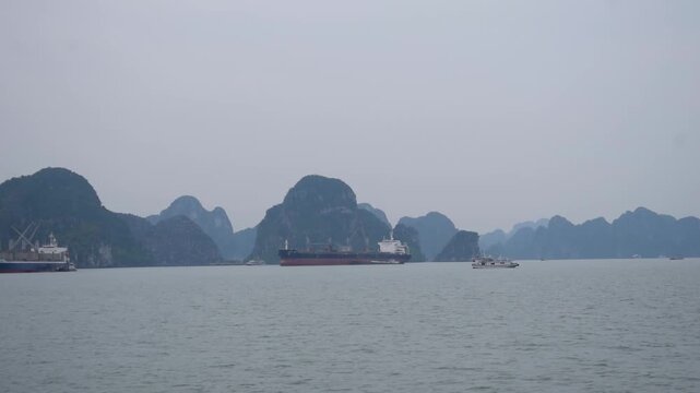 Cargo ships and tourist boats sail through calm waters surrounded by dramatic limestone karsts, showcasing tourism, maritime transport and the UNESCO landscape of Ha Long and Cat Bah, Vietnam.