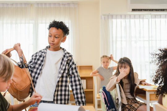 Young boy packing backpack in a school classroom with friends, Diverse elementary students in classroom preparing to leave after school, Happy multi-ethnic children finishing daily lessons