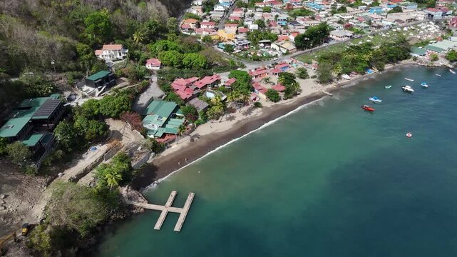 High angle drone view of a lush tropical coastline with a private boat pier and clear turquoise bay in Saint Lucia