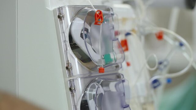 Rotating pump chambers and color-coded tubing on an operating hemodialysis machine in a hospital setting.