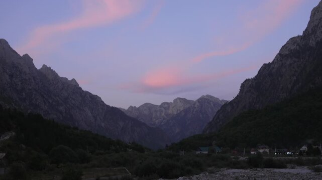 Rugged mountains cradle the tranquil Valbona Valley under a serene dusk sky with soft pink clouds drifting gently.