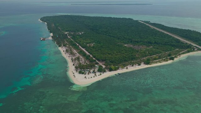 Aerial backward ascent pulling away from Candaman Island, Balabac, Palawan, Philippines. Reverse climbing drone flight reveals tropical coastline, white sandbar, and turquoise coral reef.