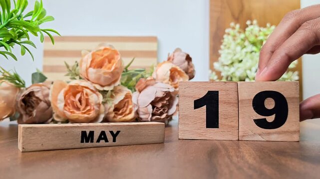 Hand placing wooden calendar blocks showing may 19 on a wooden table