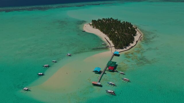 Aerial drone flight flying forward toward the wooden dock of Onuk Island, Balabac, Palawan, Philippines. Straight tracking shot over transparent turquoise ocean revealing tropical stilt resort.