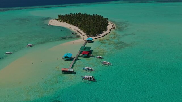 Aerial vertical descent facing the wooden dock and overwater bungalows of Onuk Island, Balabac, Philippines. Drone drops down over crystal clear turquoise sea and tropical reef.