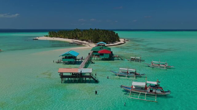 Close-up aerial drone push-in to the overwater stilt houses and wooden pier of Onuk Island, Balabac, Philippines. Low altitude forward flight over shallow transparent turquoise reef.